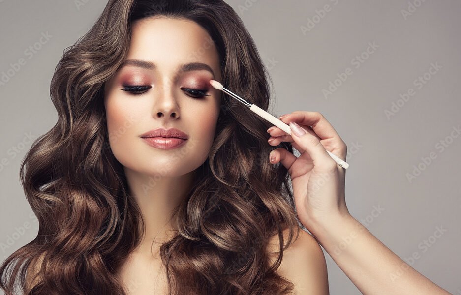 Makeup artist applies  eye shadow  . Beautiful woman with make-up face. Hand of visagiste, painting  cosmetics of young beauty  model girl . Make up in process